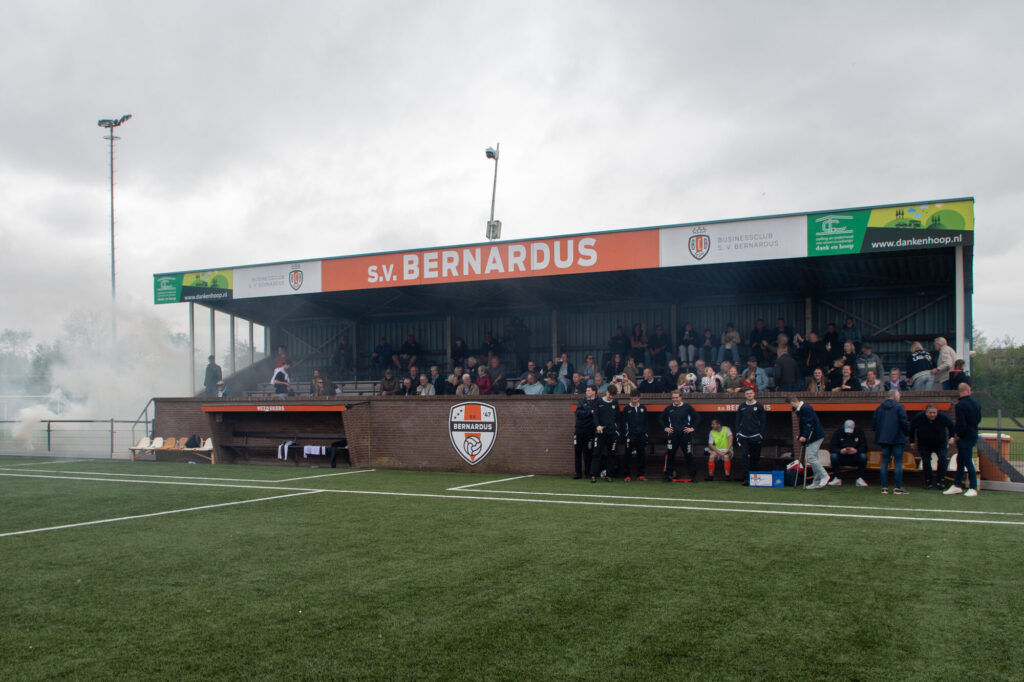 De hoofdtribune van SV Bernardus met oranje rook en publiek