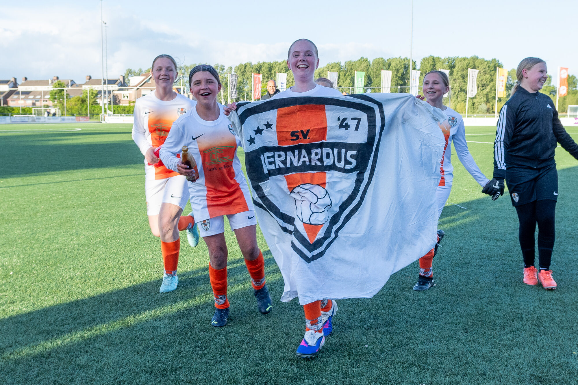 Jonge speelsters lopen juichend met de clubvlag van SV Bernardus